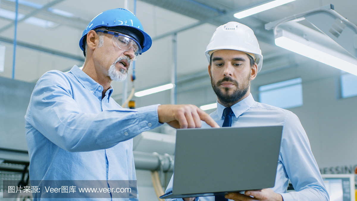 部門主管持有筆記本電腦并與總工程師討論產(chǎn)品細節(jié)。他們戴著安全帽在現(xiàn)代工廠工作。